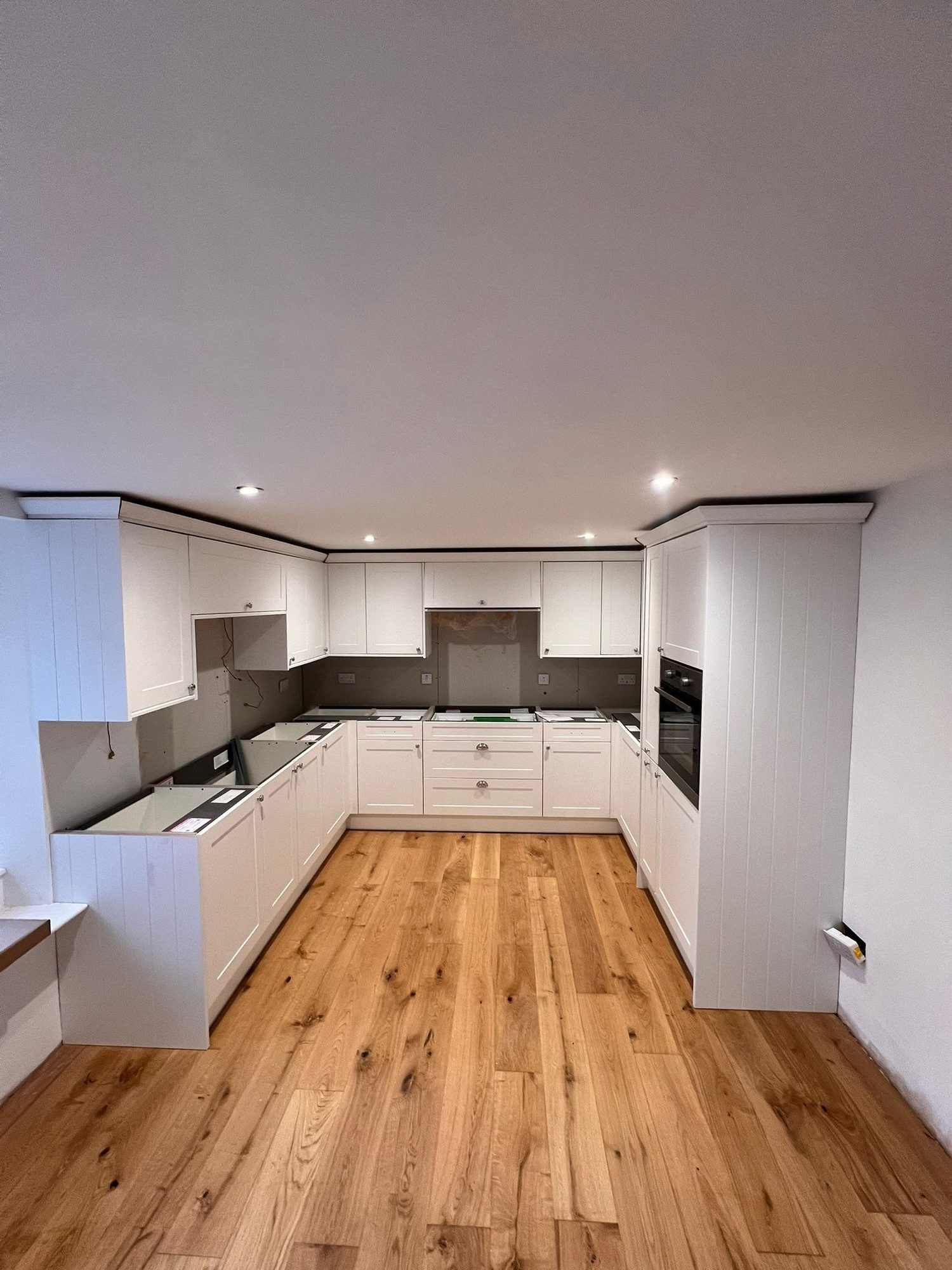 Renovated kitchen with white units and oak flooring