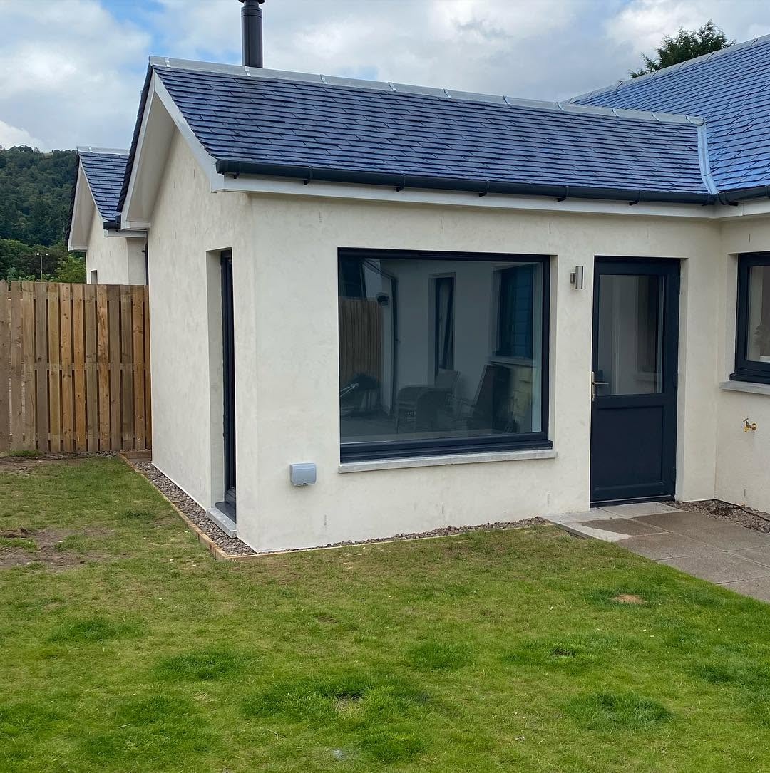 Rendered house extension with slate roof and dark-framed windows