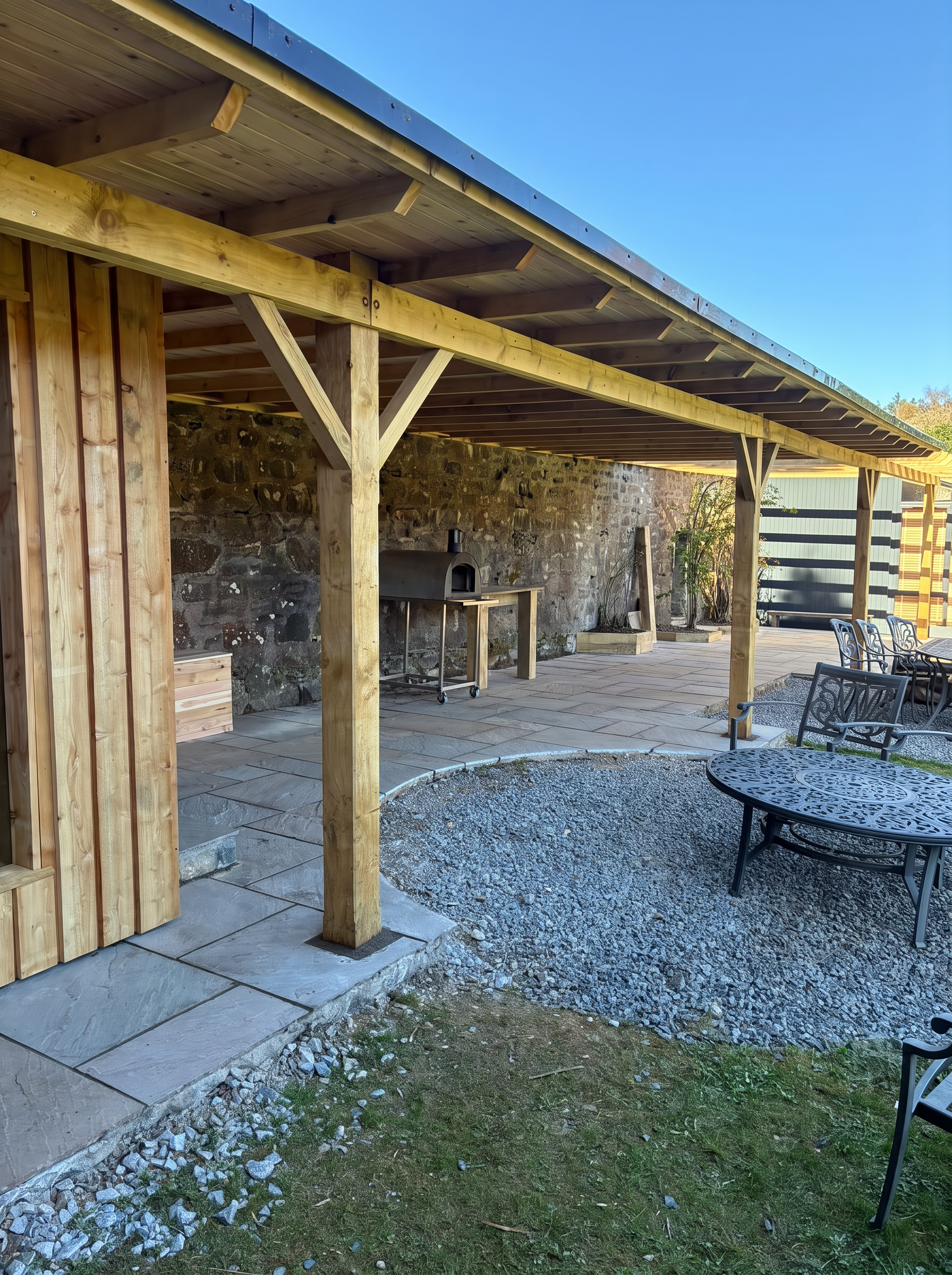 Timber-frame covered patio with exposed beams beside a stone wall