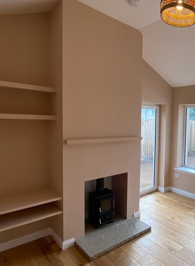 Renovated room with timber flooring, fitted shelving, wood-burning stove and garden window