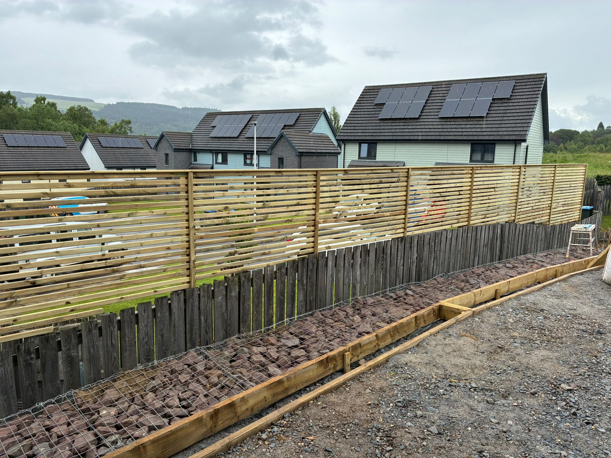 Slatted timber fencing above a gabion retaining wall