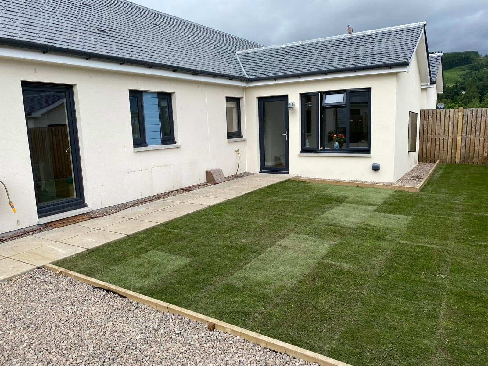 Rendered house extension with slate roof, glazed doors and landscaped lawn